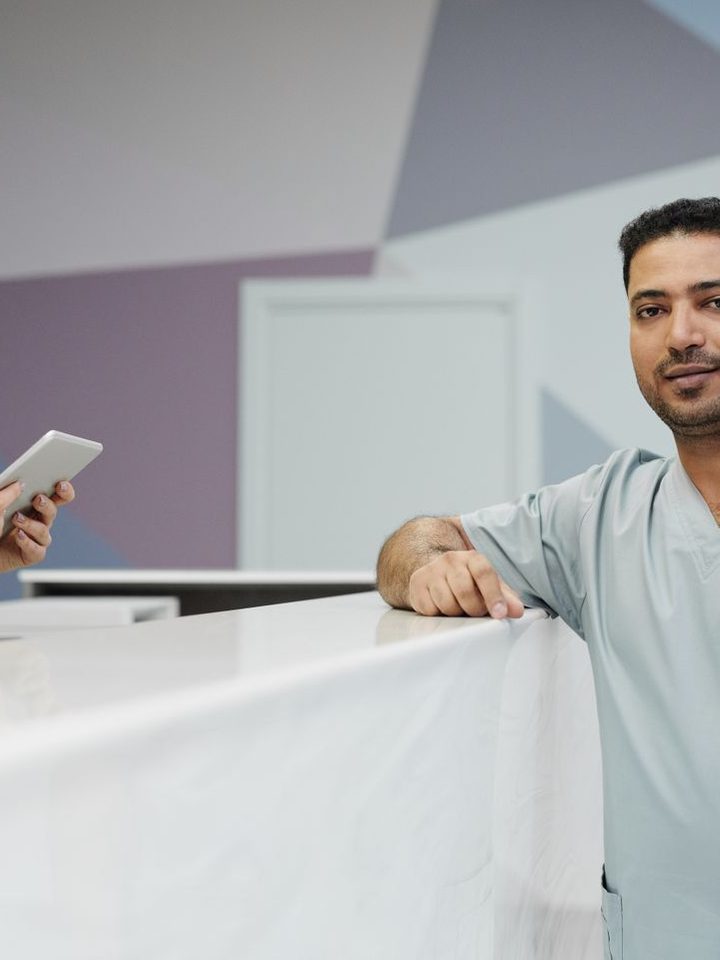 Two clinicians in scrubs at a front desk with a tablet